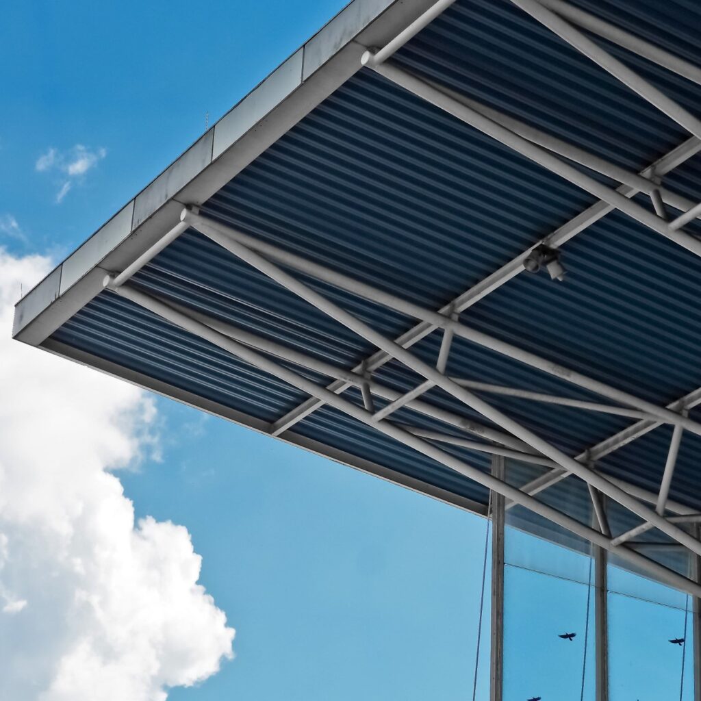 A roof of a building made of steel and composite material, with a blue sky and clouds visible in the background, showcasing architectural elements.