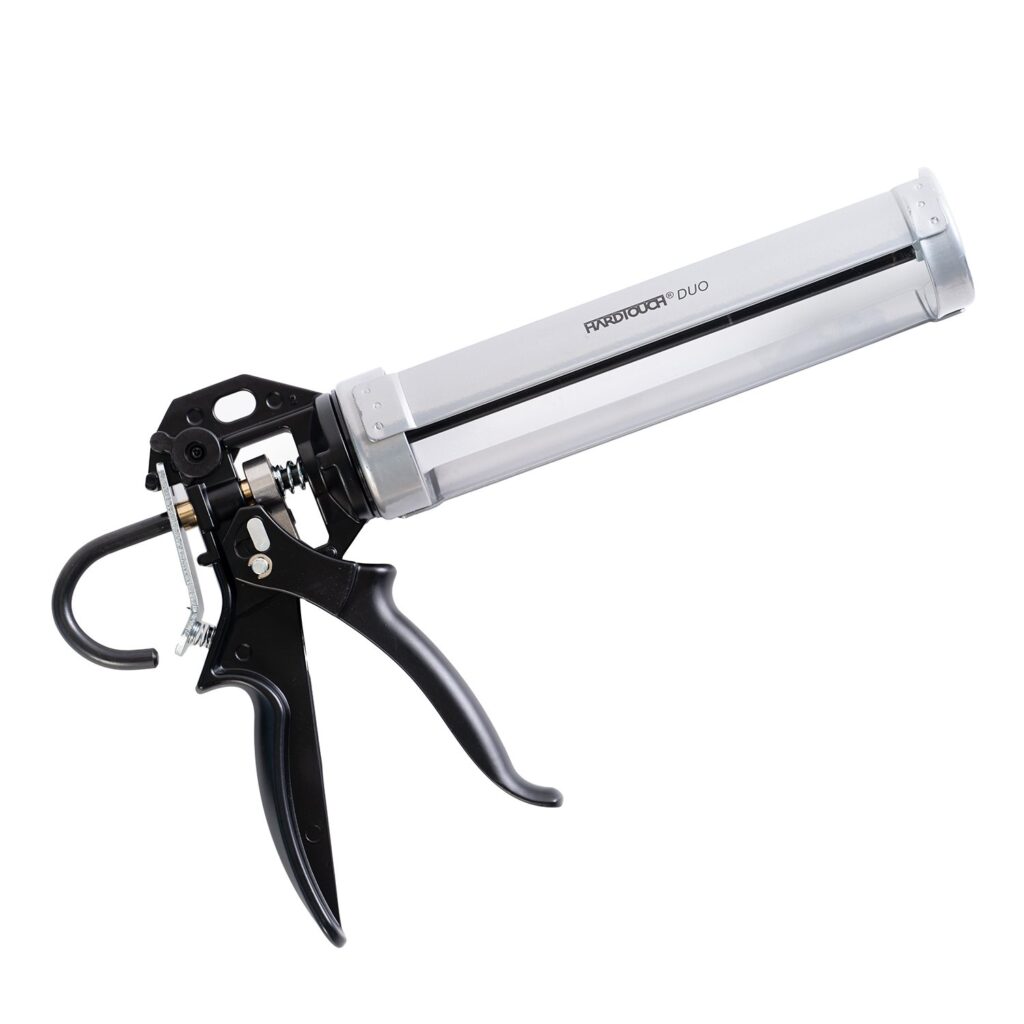 A silver and black caulking gun placed on a surface, with a pair of scissors nearby.